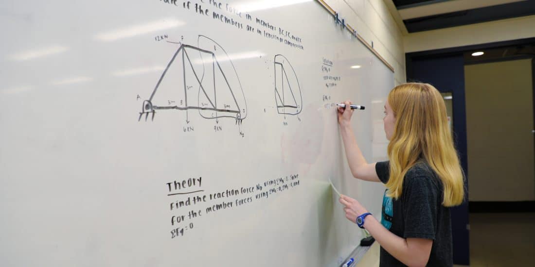A physics student running physics calculations on a whiteboard in a classroom