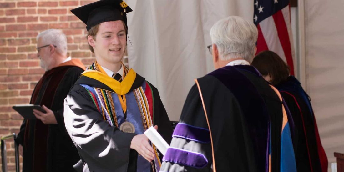 A graduate in cap and gown shakes hands with President Lindgren while receiving a diploma during the Commencement ceremony.